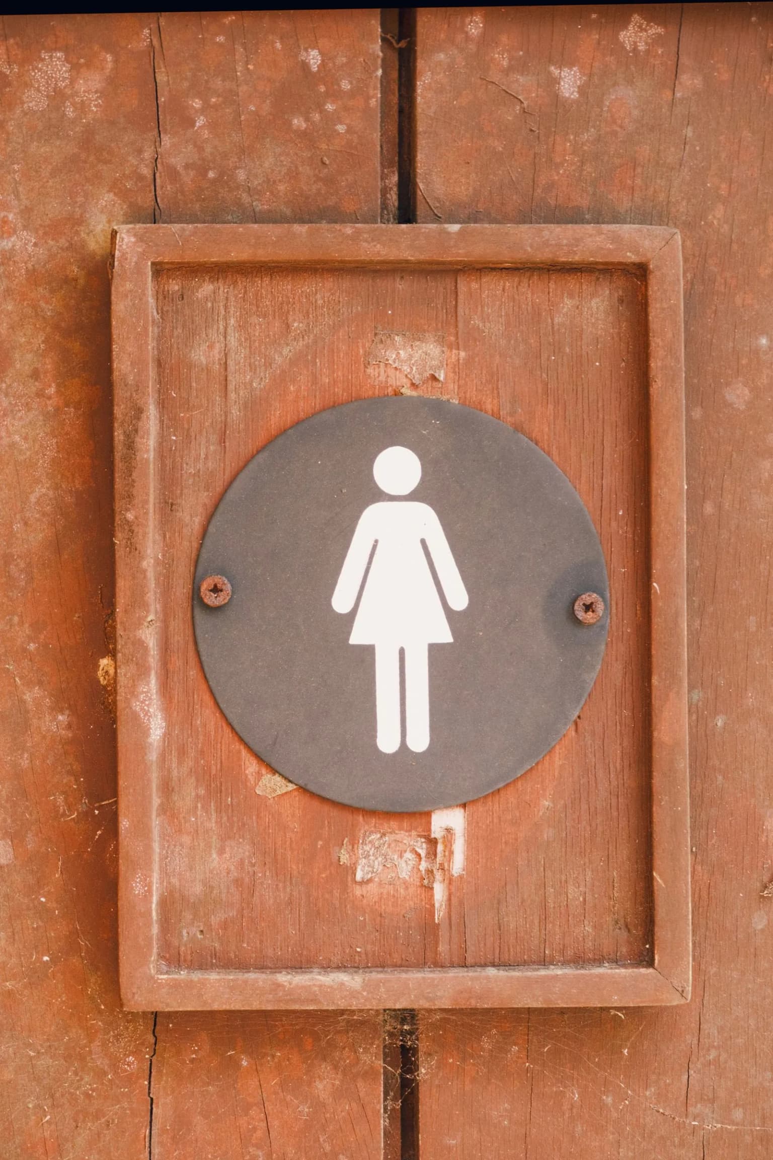 Porta de banheiro feminino em madeira, representando a urgência urinária